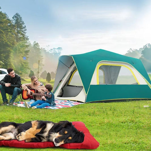 A dog lying on a red pet bed outdoors with a green tent in the background where a family is camping.

